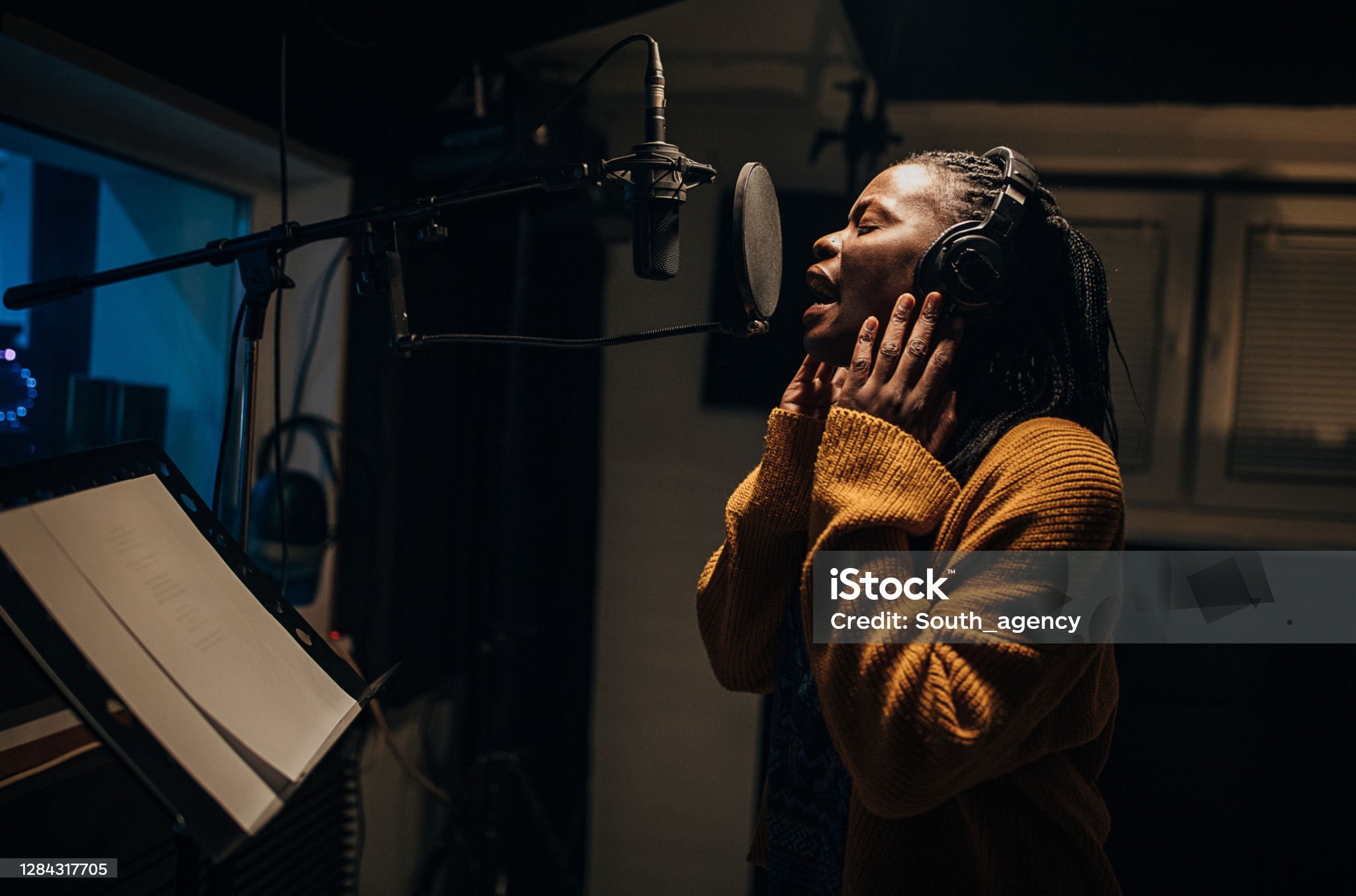 artists management One woman, beautiful black female vocalist wearing headphones and singing into microphone in recording studio.